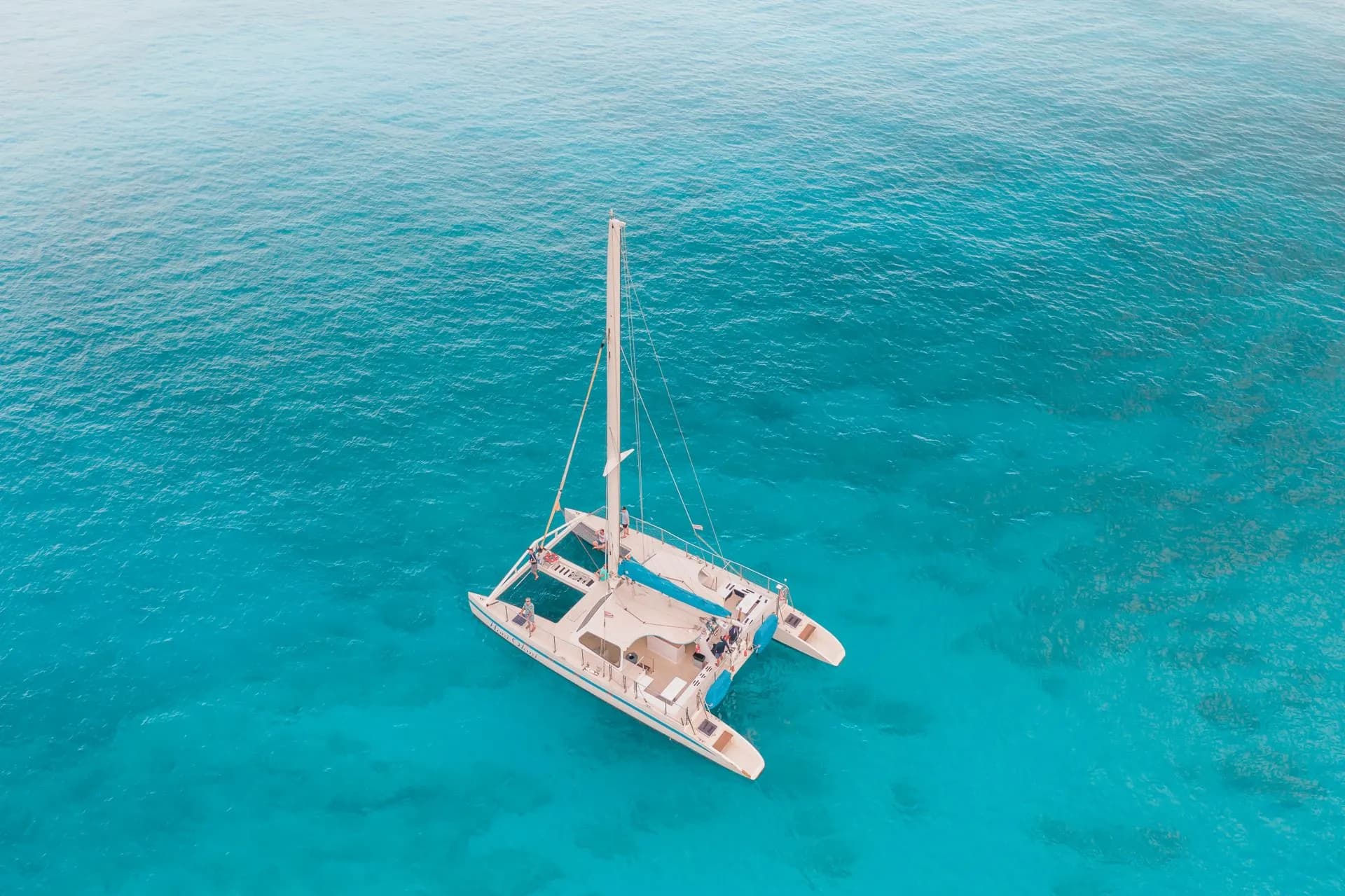 A white sailing catamaran anchored in a turquoise cove in the Bay of Palma, Mallorca, with swimmers in the water