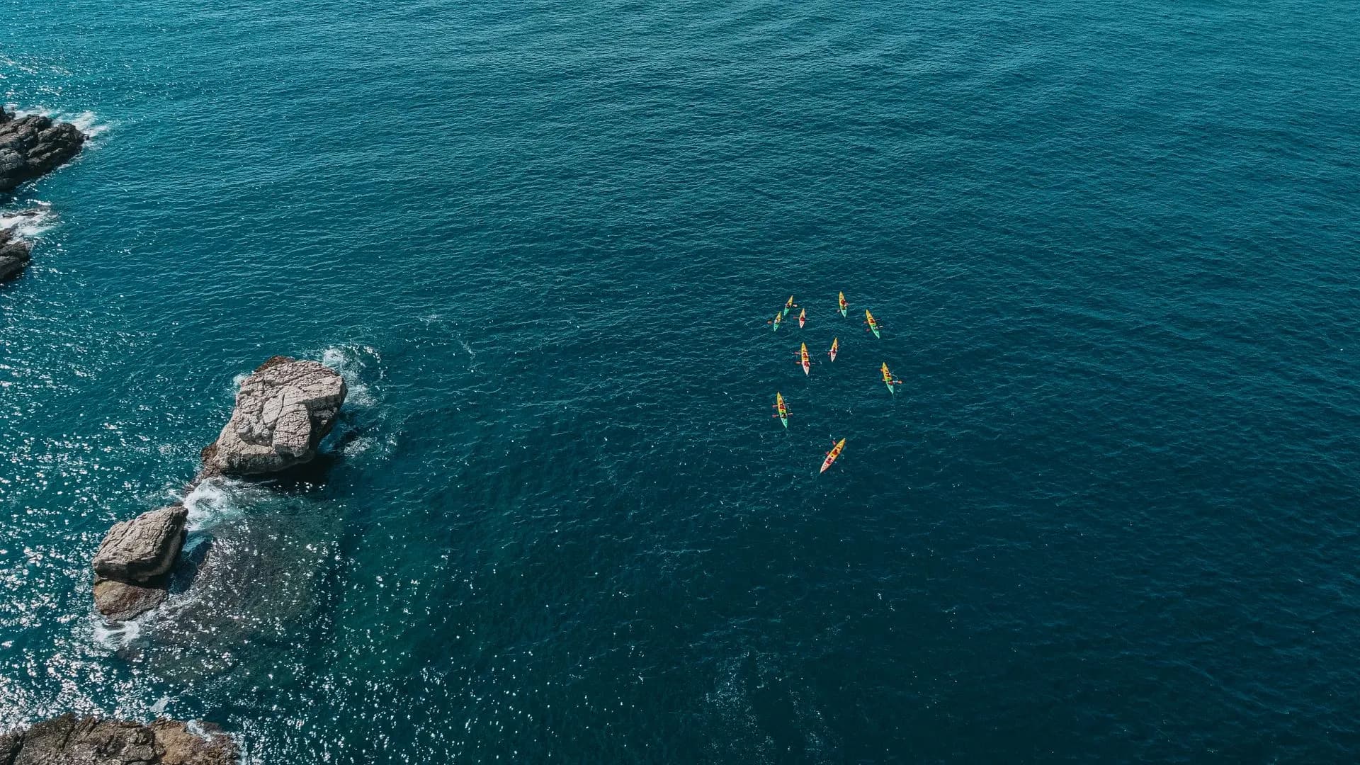 Sea kayakers paddling into a blue sea cave along the clear turquoise coast of Mallorca