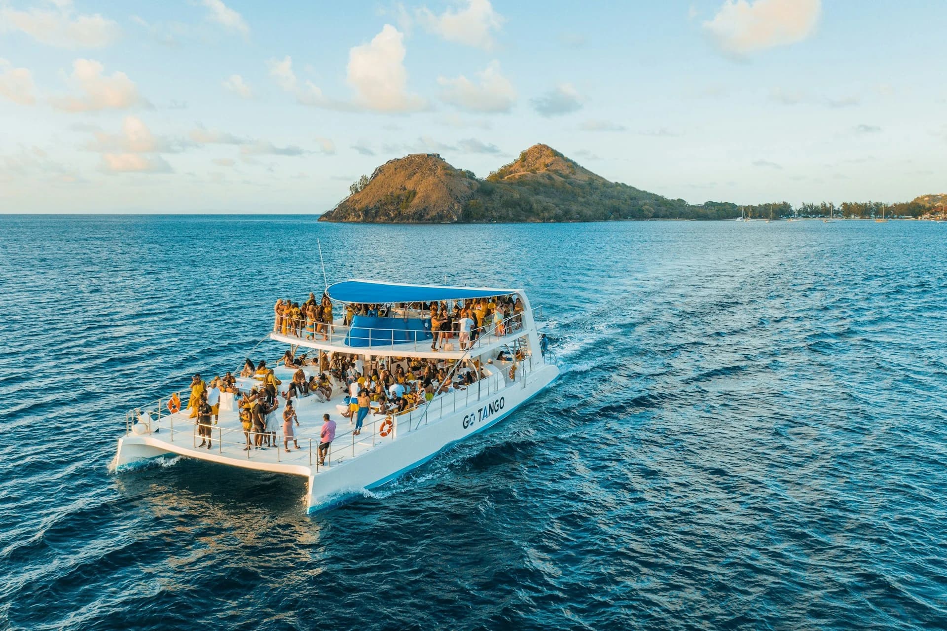 Group dancing to a DJ on a catamaran party boat off the Barcelona coast at sunset with drinks in hand