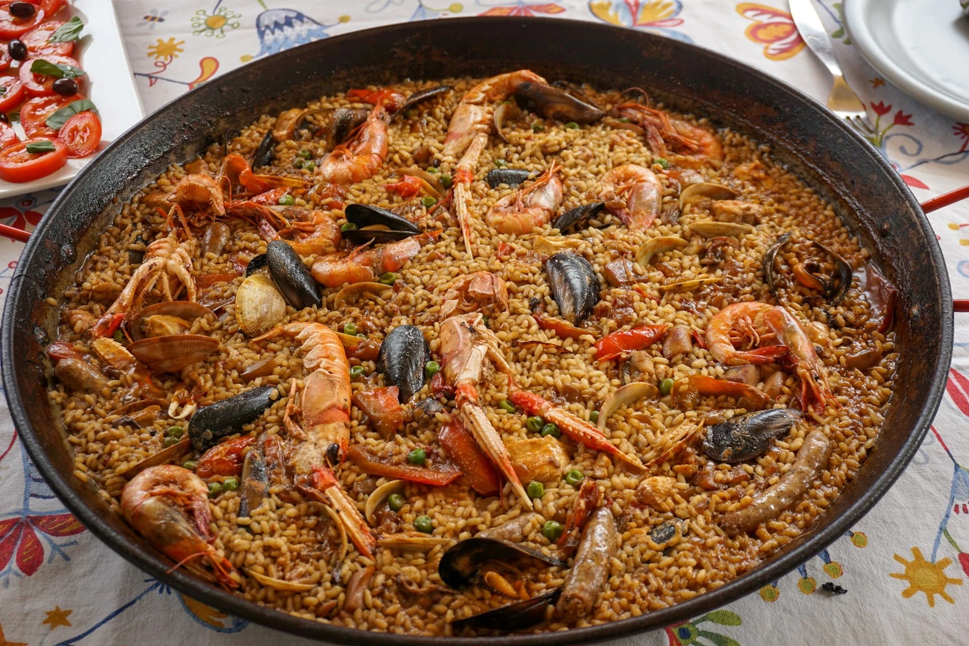 Hands stirring a paella pan with chicken, peppers, and saffron rice at a Seville cooking class