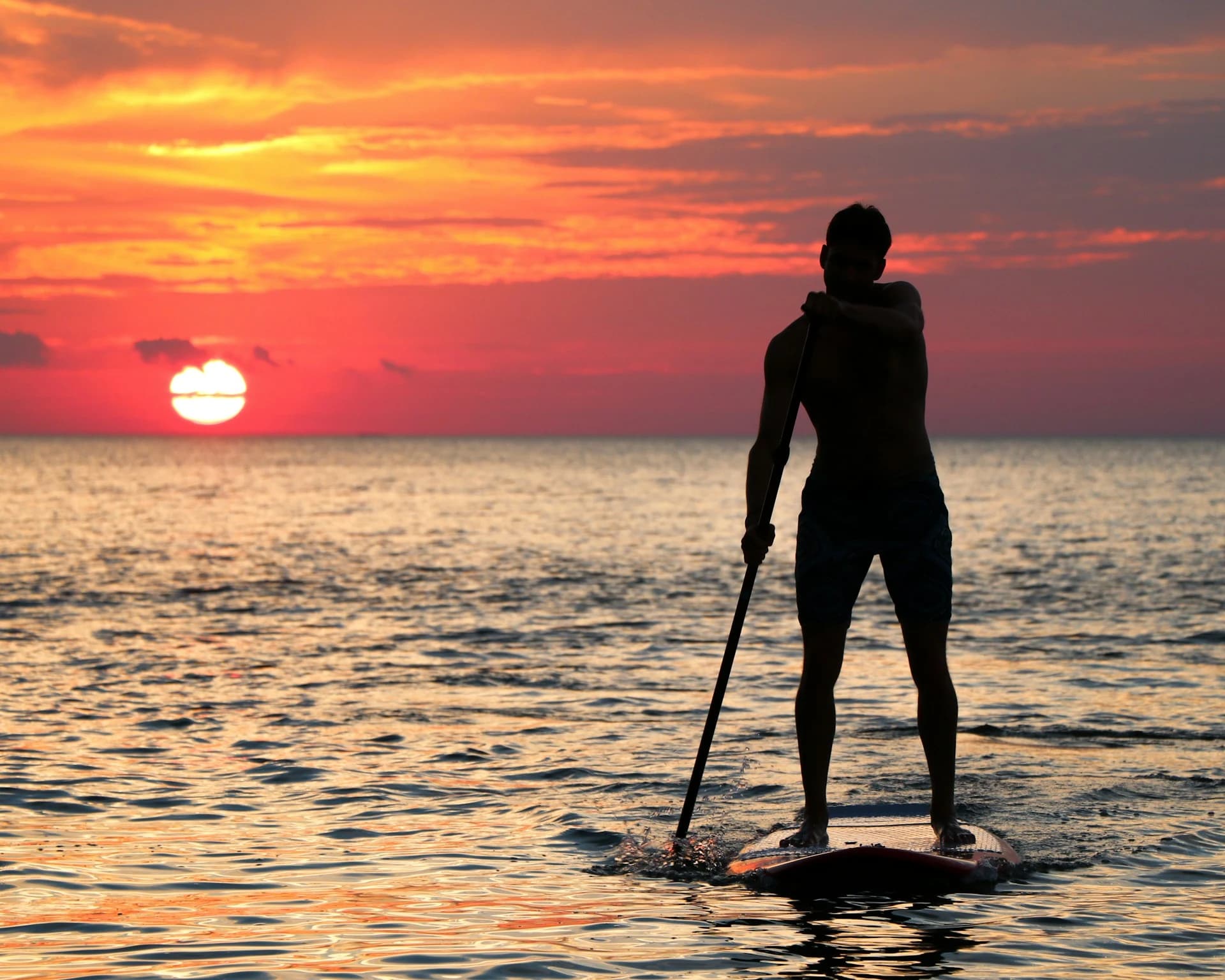 Practicantes de paddle surf en agua tranquila frente a la playa de la Barceloneta al amanecer, con el perfil de Barcelona detrás